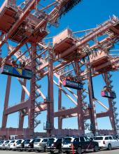 Three containers hang from cranes at Terminal 46 in Seattle. The middle container has a “Welcome to the Pacific Northwest” message to FIFA World Cup visitors, while the outside containers have Bosnia-Herzegovina and Qatar flags.