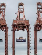 Three containers hang from cranes at Terminal 46 in Seattle. The middle container has a “Welcome to the Pacific Northwest” message to FIFA World Cup visitors, while the outside containers have the Egypt and IR Iran flags.