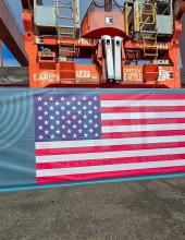 A shipping container with a United States flag banner at Terminal 46 before it is hung from a crane. 
