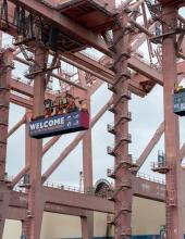 Three containers hang from cranes at Terminal 46 in Seattle. The middle container has a “Welcome to the Pacific Northwest” message to FIFA World Cup visitors, while the outside containers have the Belgium and Senegal flags.