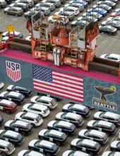 A shipping container with a United States flag banner hangs from a crane at Terminal 46 in Seattle.