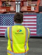 A Northwest Seaport Alliance staff member looks at shipping container with a United States flag banner attached before it is raised above Terminal 46 in Seattle.